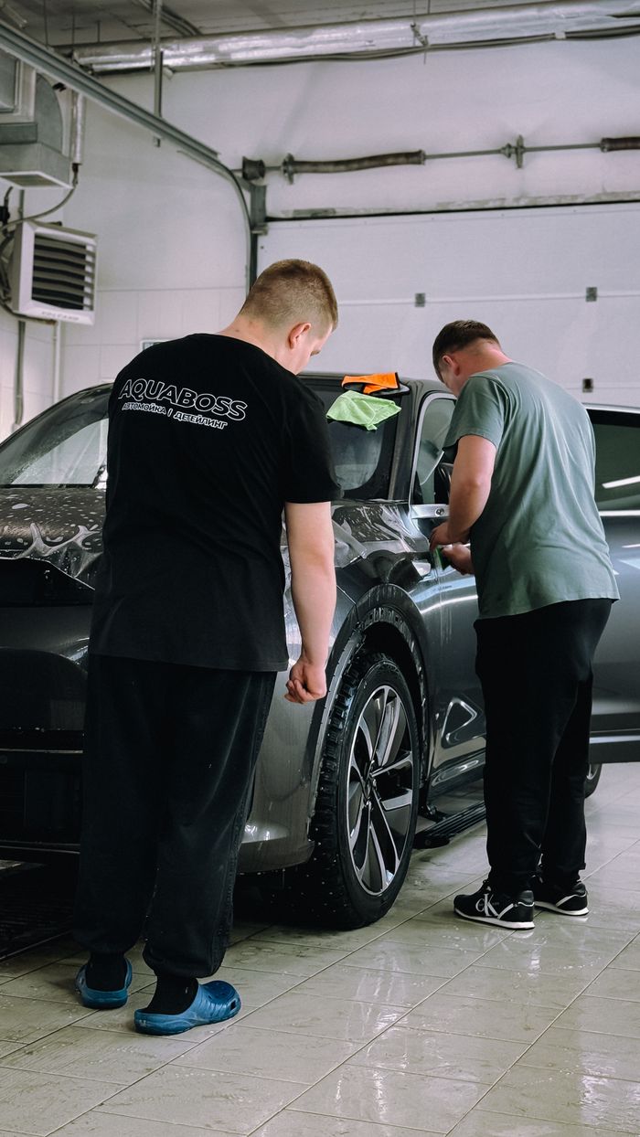 Two men detailing a car in an indoor workshop, focusing on precision and care.