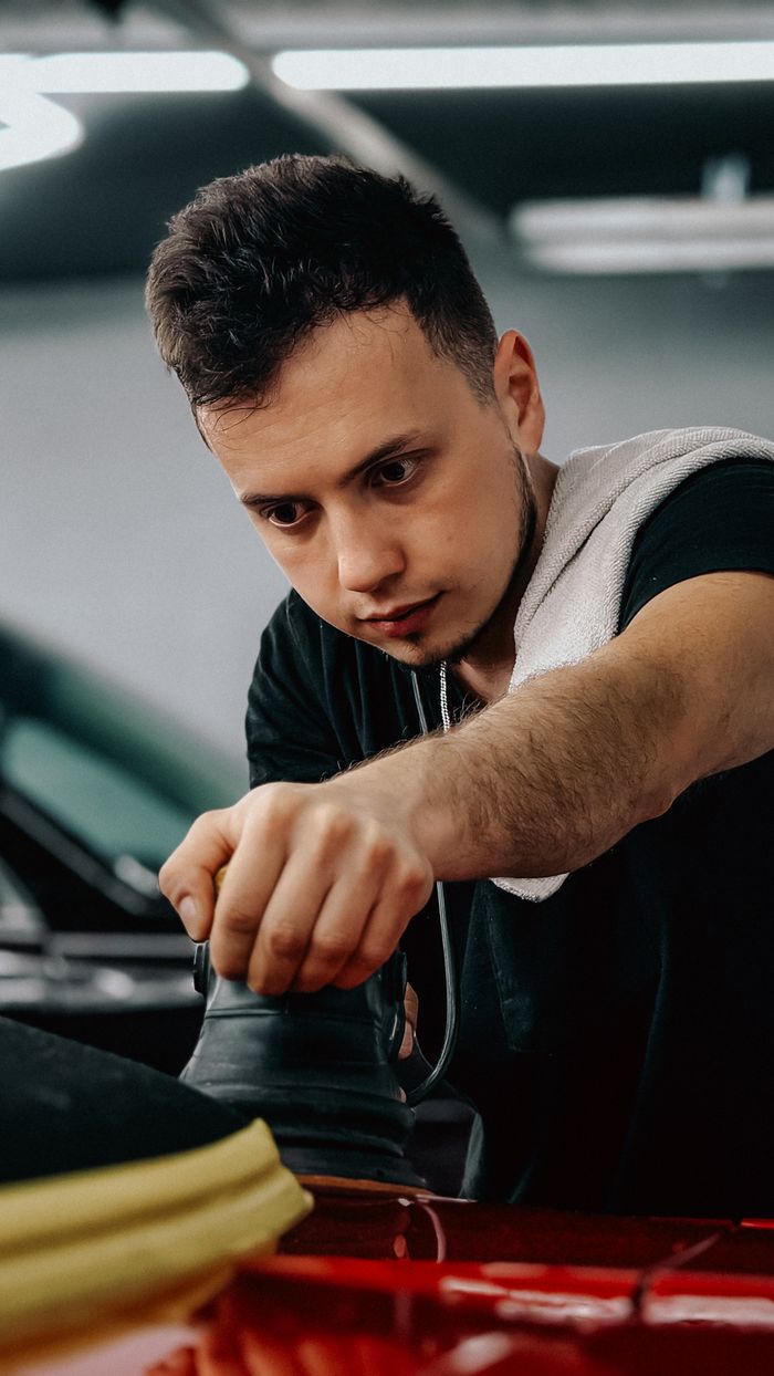 Young man working meticulously on car detailing indoors with professional equipment.